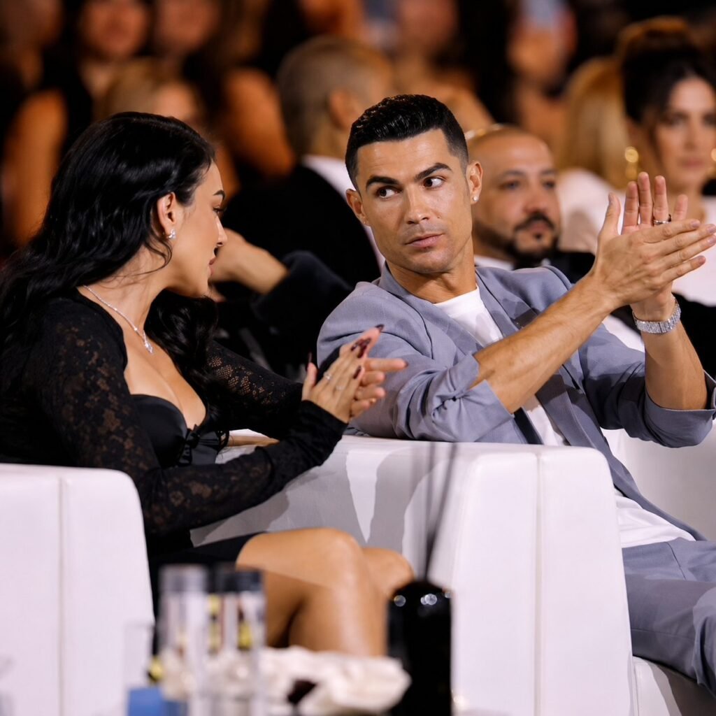 Cristiano Ronaldo and Georgina Rodriguez seated in white armchairs at an awards ceremony, both applauding.