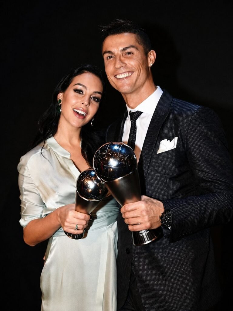 Cristiano Ronaldo and Georgina Rodriguez each holding a football trophy against a black backdrop.